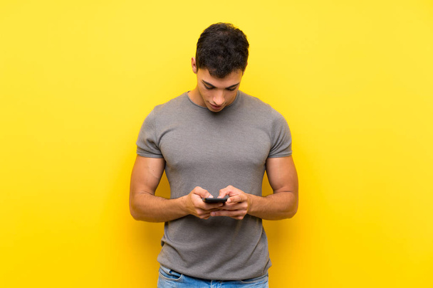 Handsome man over isolated yellow wall sending a message with the mobile - Photo, Image