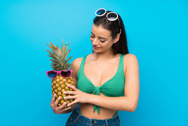 Young woman in swimsuit in summer holidays holding a pineapple with sunglasses - Фото, зображення