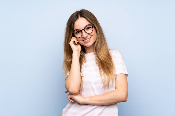Young woman over isolated blue background with glasses and happy - Foto, afbeelding