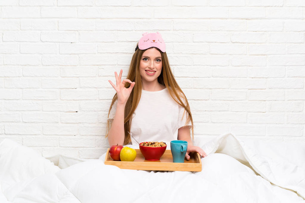 Young woman in dressing gown with breakfast showing an ok sign with fingers - Fotó, kép