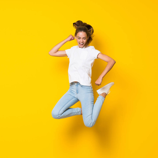 Young woman jumping over isolated yellow wall - Фото, изображение