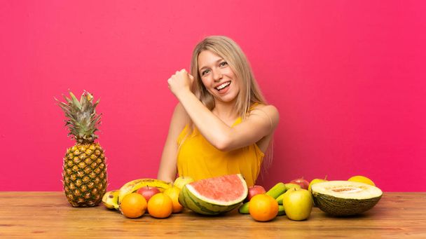 Young blonde woman with lots of fruits celebrating a victory - Photo, Image