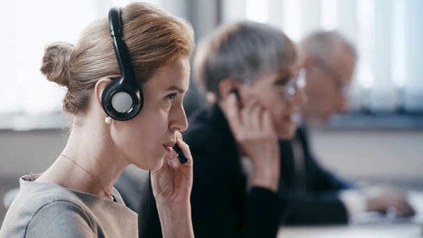 επιλεκτική εστίαση της ελκυστικής γυναίκας στα ακουστικά που μιλούν ενώ συμβουλεύονται και χαμογελούν κοντά σε συναδέλφους  - Πλάνα, βίντεο