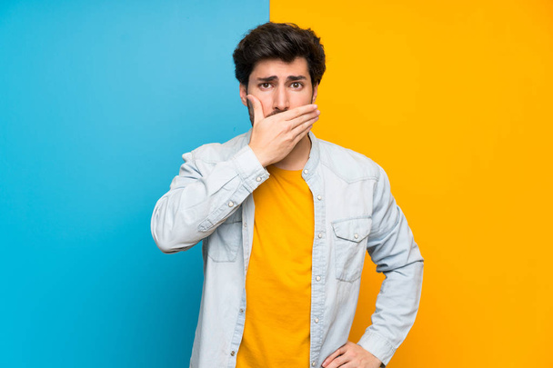 Handsome over isolated colorful background covering mouth with hands - Foto, imagen