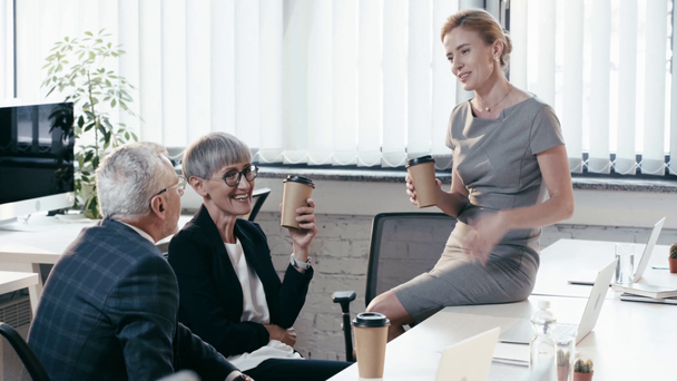 businesswoman sitting on table and talking with coworkers smiling, gesturing and drinking coffee to go  - Footage, Video