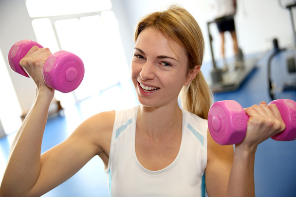 Happy woman in gym lifting dumbbells - Foto, imagen