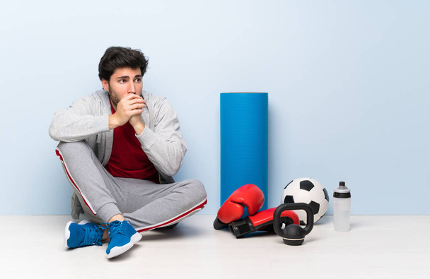 Sport man sitting on the floor covering mouth and looking to the side - Фото, зображення