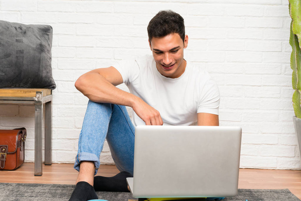 Handsome man sitting on the floor with his laptop - Фото, изображение