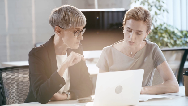 mulher de negócios em óculos usando laptop, olhando para belos colegas de trabalho com papel, falando e gesticulando no escritório
  - Filmagem, Vídeo