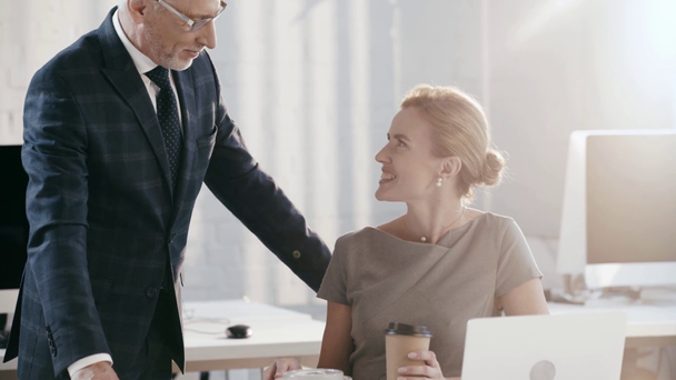 όμορφος επιχειρηματίας σε γυαλιά βάζοντας πλαστικό δοχείο και χάρτινο φλιτζάνι κοντά ελκυστική και χαρούμενη επιχειρηματίας  - Πλάνα, βίντεο
