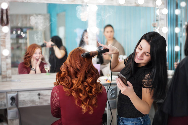 Comic photo in a beauty salon. The hairdresser looks into the phone and the client's hair is on fire. - Photo, Image