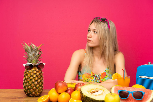 Jovem mulher loira com muitas frutas olhando lado
 - Foto, Imagem