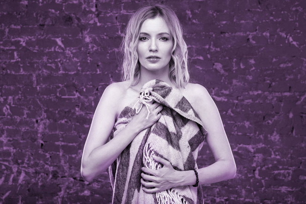 Portrait of a young sexy female fashion model in wool blanket on brick wall background. Photo tinted in purple. - Φωτογραφία, εικόνα
