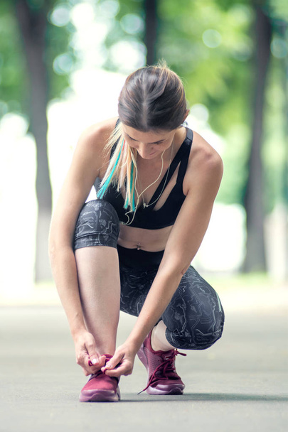 Widok z przodu kobieta jest wiązanie sznurowadła przed runing w parku miejskim. Koncepcja fitness i styl życia. - Zdjęcie, obraz