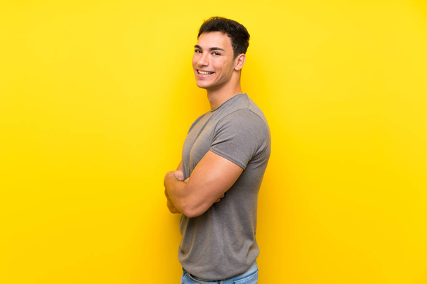 Handsome man over isolated yellow wall with arms crossed and looking forward - Photo, Image