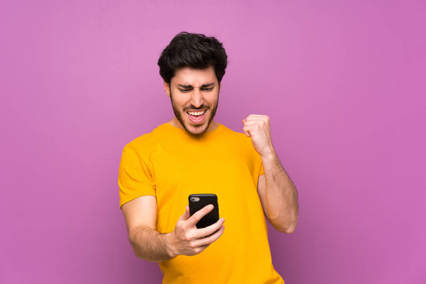 Handsome over isolated purple wall with phone in victory position - Zdjęcie, obraz