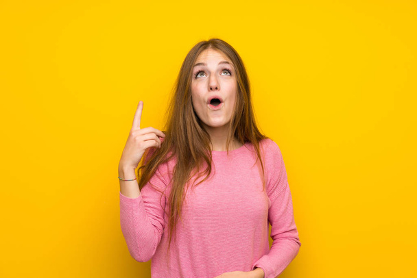 Young woman with long hair over isolated yellow wall pointing up and surprised - Photo, Image