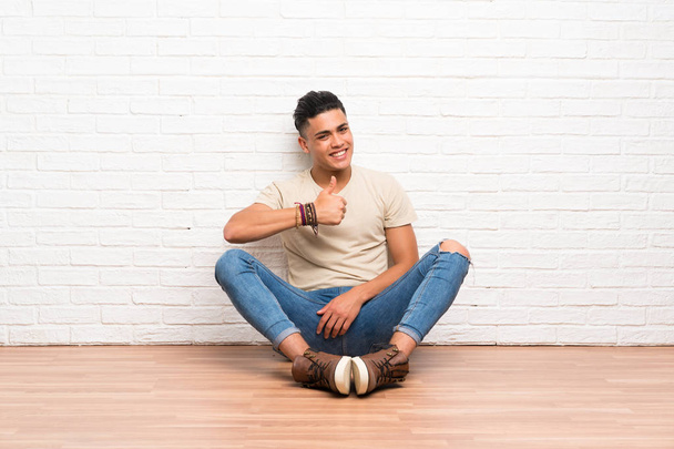 Jeune homme assis sur le sol donnant un pouce geste - Photo, image