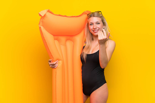 Młoda kobieta w stroju kąpielową na żółtym tle prezentując i zapraszając przyjść - Zdjęcie, obraz