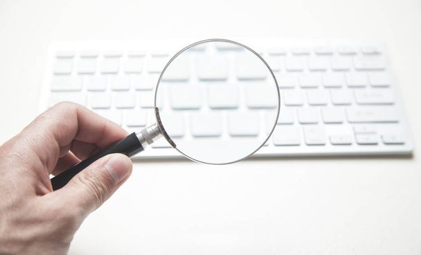 Hand holding magnifying glass with computer keyboard. Searching  - Photo, Image