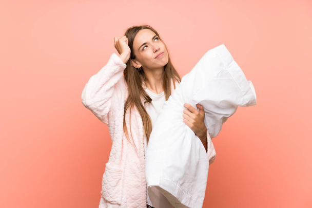 Young woman in dressing gown over pink wall having doubts and with confuse face expression - Photo, Image