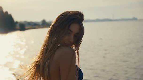 Retrato de una joven seductora con el pelo largo en bikini posando al atardecer en la playa
 - Metraje, vídeo