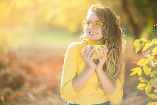 Retrato de close-up de jovem mulher bonita no fundo do outono com xícara de café. Feminino no fundo da queda ao ar livre
. - Foto, Imagem