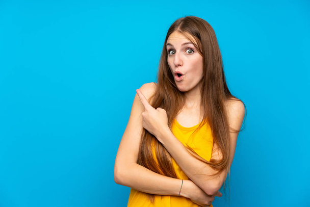 Young woman with long hair over isolated blue wall surprised and pointing side - Foto, immagini