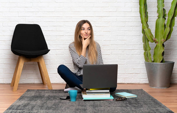 Nuori nainen istuu lattialla hänen kannettava tietokone ajattelee idea
 - Valokuva, kuva
