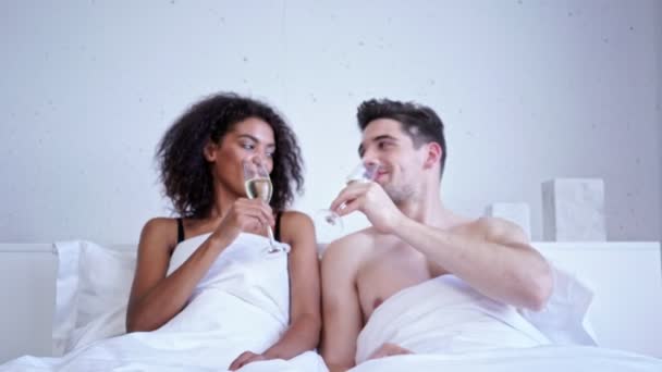 Romantic loving multiethnic couple drinking champagne while lying in bed - Metraje, vídeo