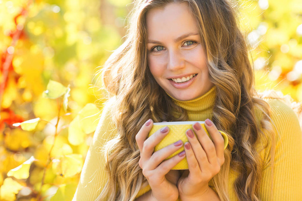 コーヒーのカップと秋の背景に若い美しい女性のクローズアップ肖像画。屋外の秋の背景に女性. - 写真・画像