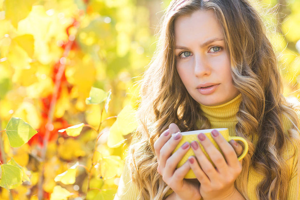 Primer plano retrato de la joven hermosa mujer en el fondo de otoño con taza de café. Mujer sobre fondo de otoño al aire libre
. - Foto, Imagen
