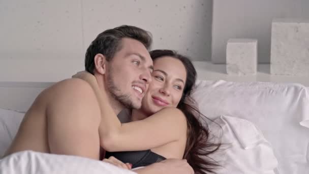 Happy loving couple embracing while lying together in bed at home - Filmati, video