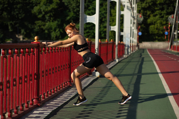 Merry athletic woman doing stretching workout at the bridge in s - Photo, Image