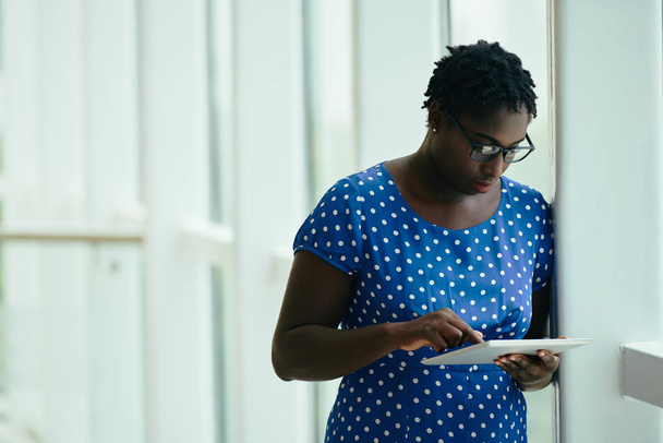 Femme entrepreneur noire dans des lunettes document de vérification sur sa tablette numérique
 - Photo, image