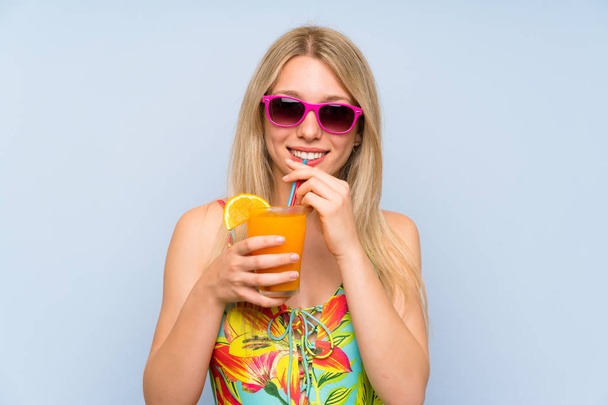Young woman in swimsuit over blue background with a cocktail - Photo, Image