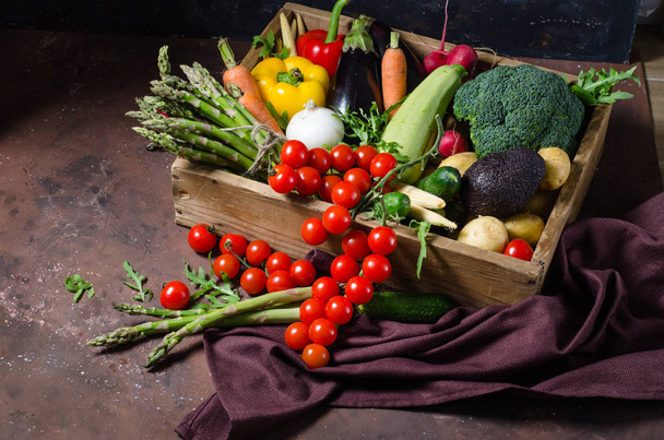 Pudełko z warzywami w gospodarstwie na ciemnym tle. Miejsce na tekst. Pomidory wiśniowe, szparagi, brokuły, papryka, bakalie, cukinia, marchew i cebula. - Zdjęcie, obraz