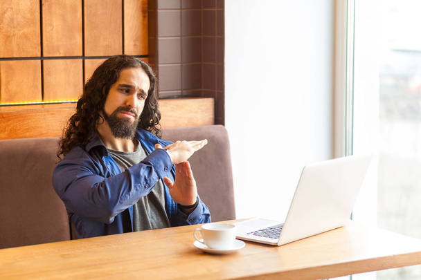 serious handsome man freelancer in casual style sitting in cafe and talking with  friend in laptop while showing stop gesture with hands - Foto, Bild