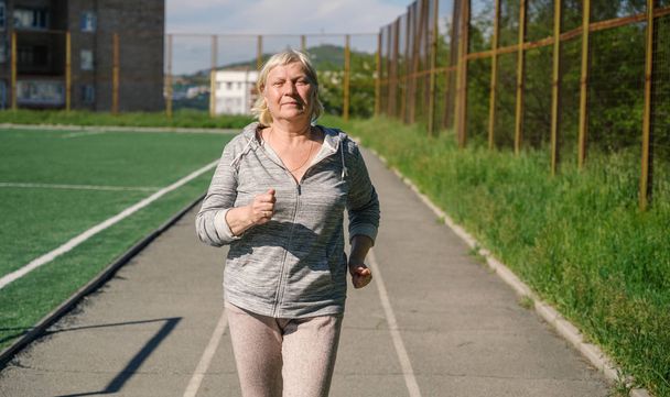 Aged woman jogging in public stadium. - Foto, Imagen