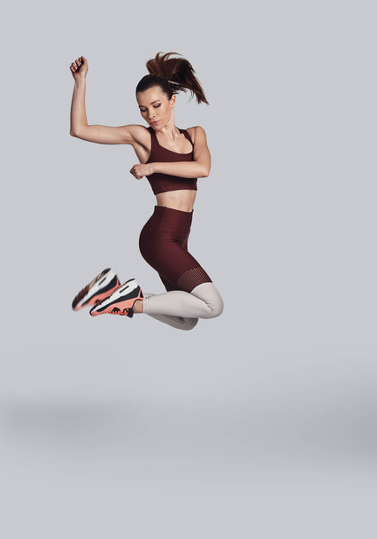 Özgürlüğü hissetmek. Gri arka plan aleyhine egzersiz yaparken spor giyim atlama çekici genç kadın tam uzunlukta - Fotoğraf, Görsel