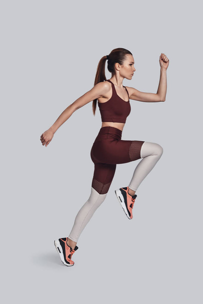 Siempre en buena forma. Longitud completa de atractiva mujer joven en ropa deportiva saltando mientras hace ejercicio sobre fondo gris
 - Foto, imagen