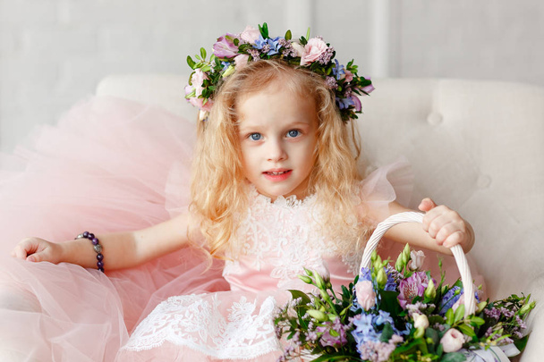 Large portrait of a cute little girl in a wreath of flowers and a beautiful bouquet of flowers in a bright studio - Photo, image