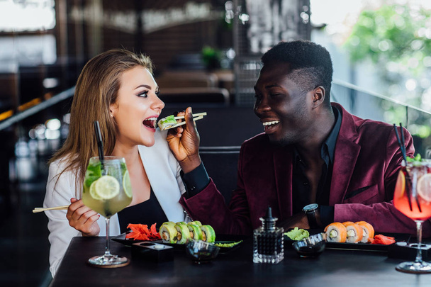 Boyfriend with his girlfriend eating sushi rolls in restaurant in modern  summer terrace. - Photo, Image