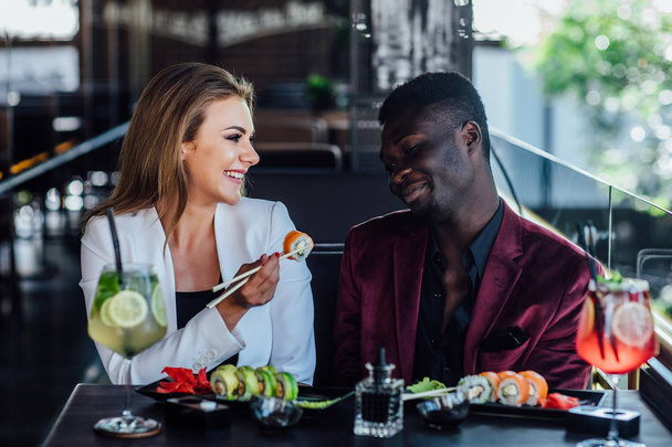 Ystävyyttä. Poikaystävä tyttöystävänsä kanssa syö sushia rullina ravintolassa modernilla kesäterassilla
. - Valokuva, kuva