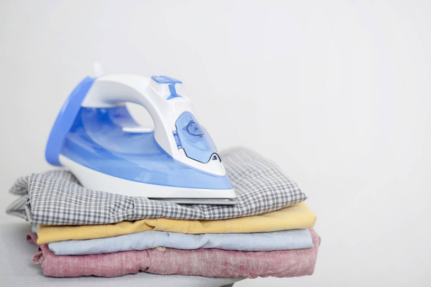 Electric iron and pile of clean clothes shirts variety of colors on ironing board. Leave space to write side text. - Photo, Image