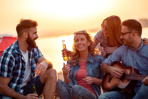 Grupo de amigos animados se divertindo na praia, tocando guitarra
. - Foto, Imagem