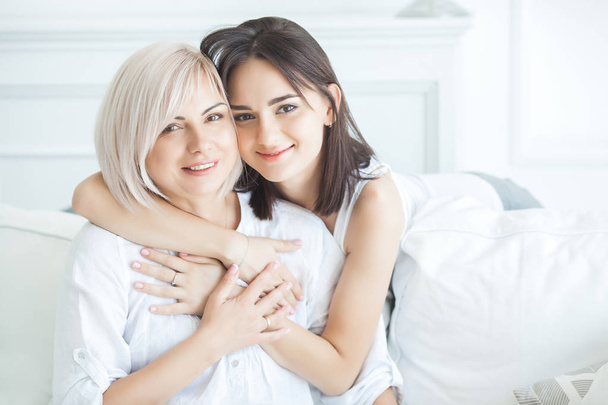 Retrato de close-up de duas mulheres bonitas mãe e filha. Mãe adulta média abraçando sua filha adulta dentro de casa. Feliz sorridente mulheres abraçando
. - Foto, Imagem