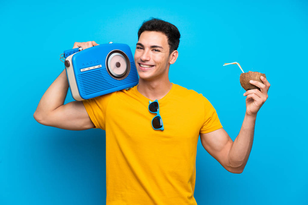 Handsome man over blue background holding a radio - Foto, afbeelding