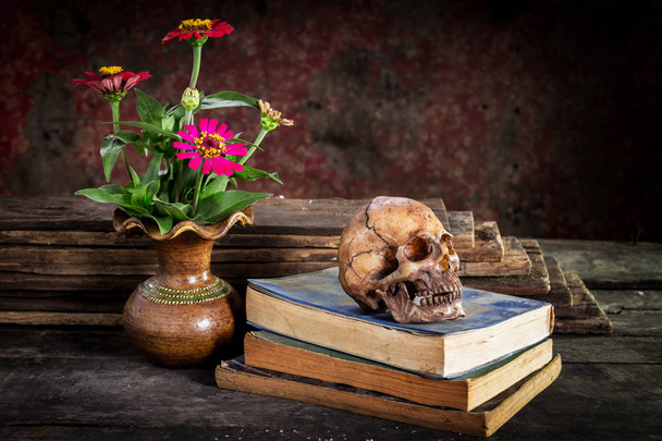 Natureza morta com crânio e livro, vaso de flores na mesa de madeira
 - Foto, Imagem