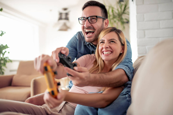 Couple in love enjoying their free time, sitting on a couch, playing video games and having fun. - Foto, Imagen